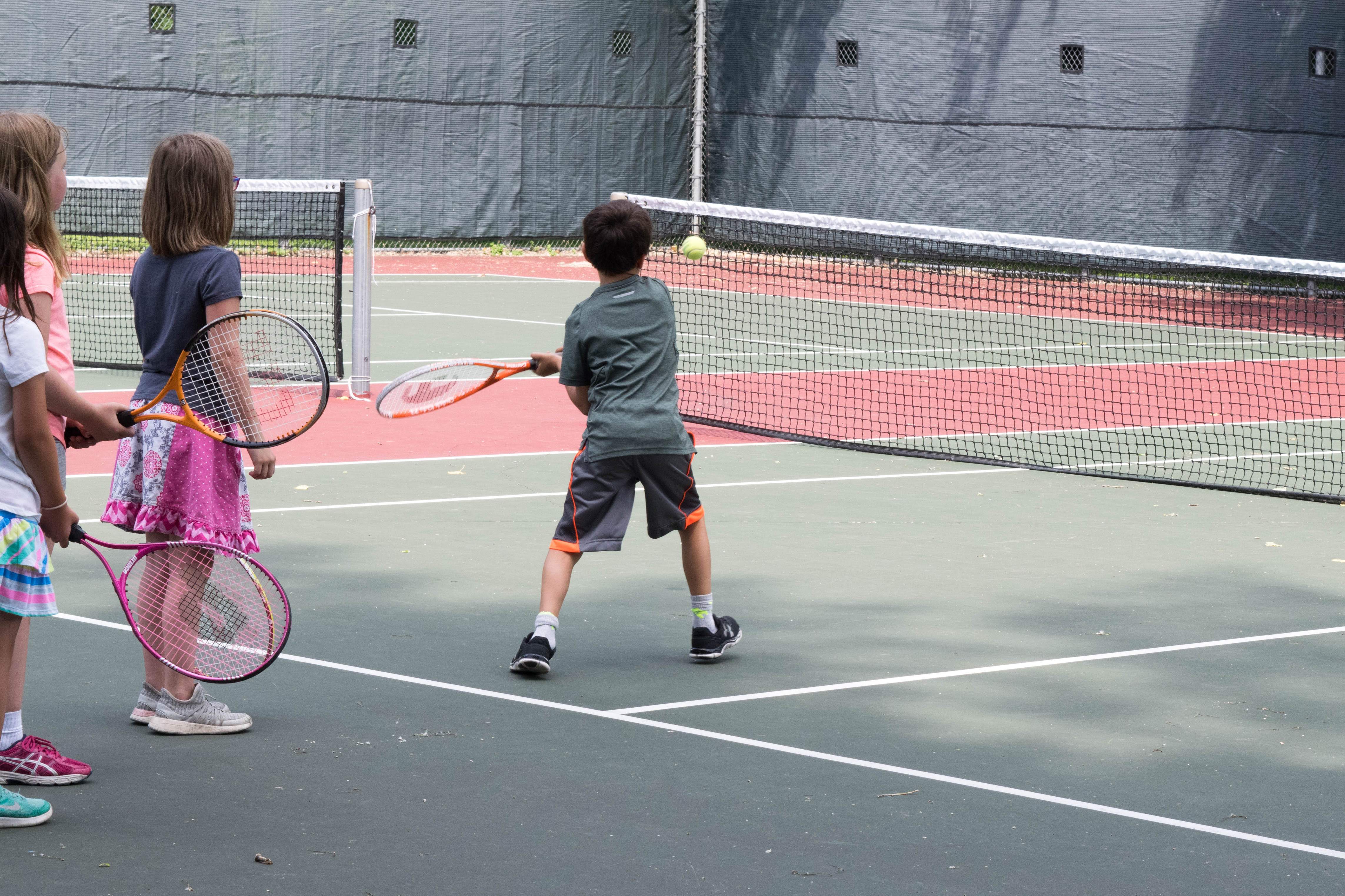 a group of kids playing tennis at an outdoor court