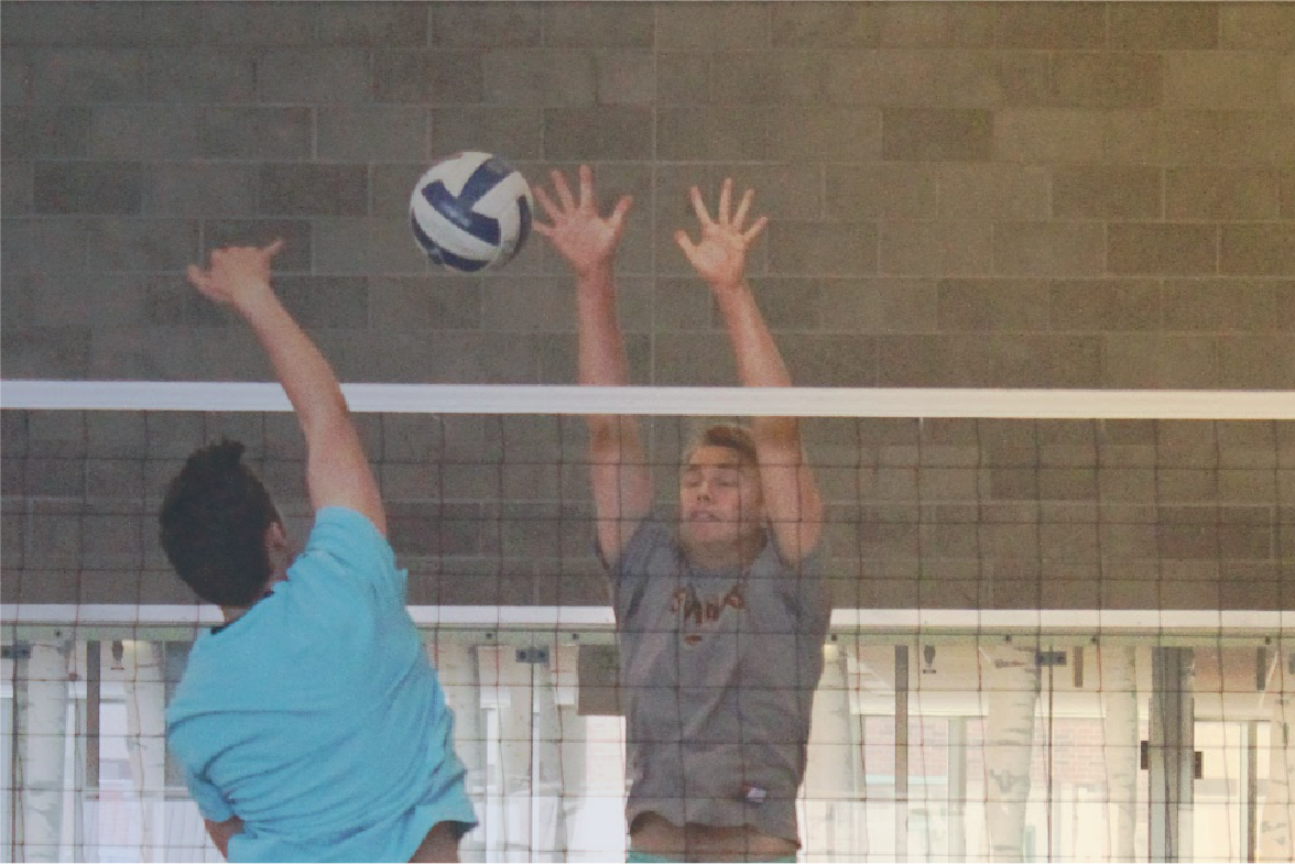 man jumping to hitting volleyball over net, another man jumping to block it